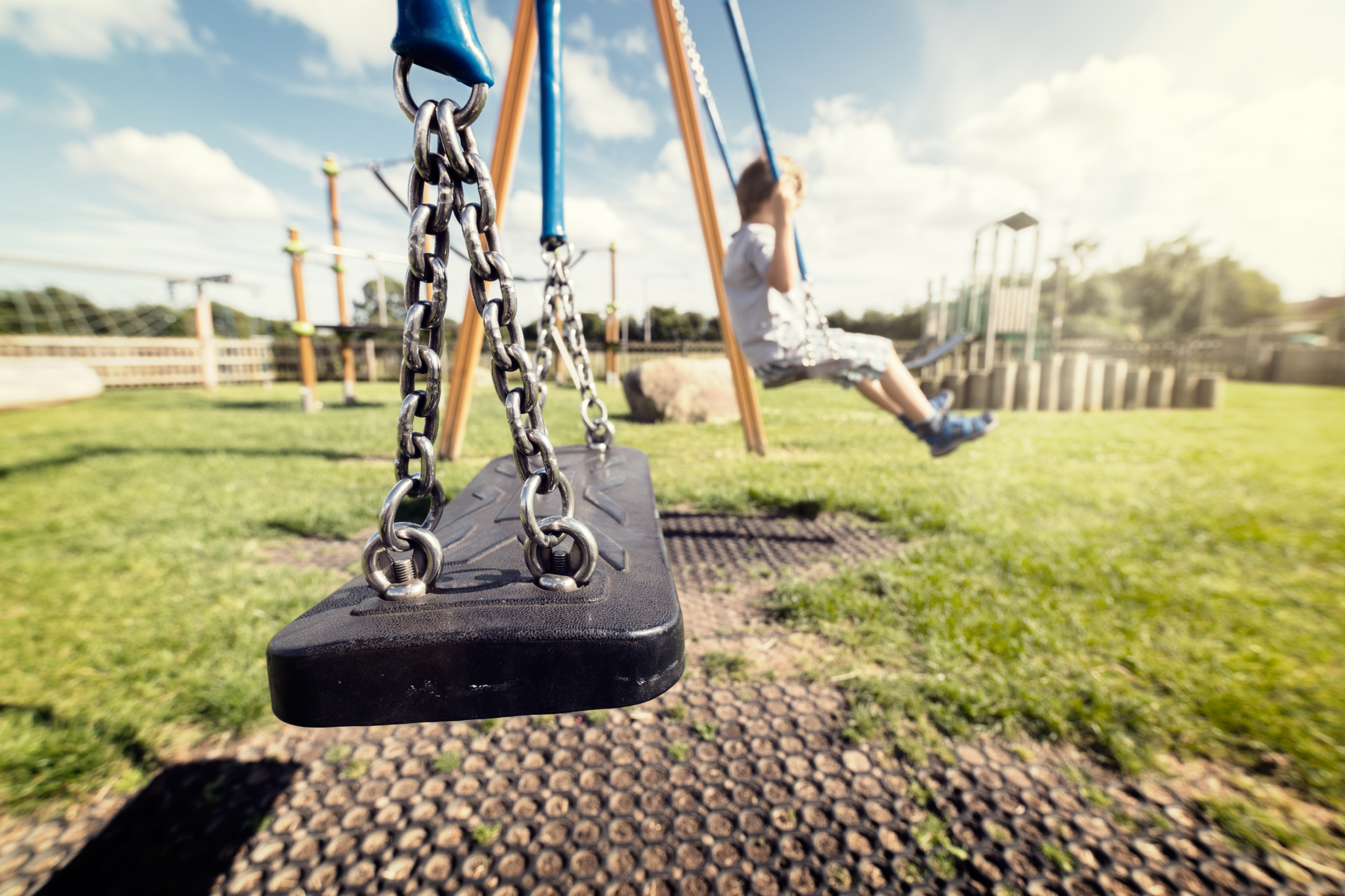 Empty playground swing with children playing in the background concept for child protection, abduction or loneliness